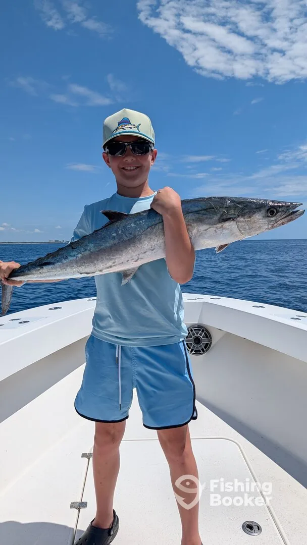 Young angler holding a king mackerel against open sky