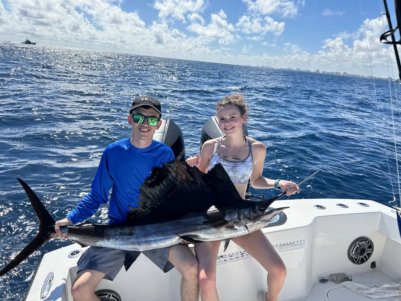 Two anglers holding a sailfish in blue water off Pompano Beach