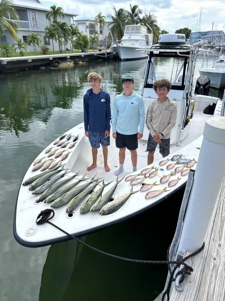 Three young anglers with a spread of mahi mahi and snapper laid out on the bow